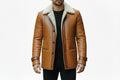 Men's grand thread adventure style genuine soft lambskin real leather long coat in burnished tan featuring a plush wide cream shearling fleece collar and notch lapels, dark brown leather piping trim, single-breasted button front closure, deep angled side handwarmer pockets, buckled sleeve cuff straps, long fitted sleeves, mid-to-thigh length cut, and custom made-to-measure fitting across the UK, USA, and Australia.
