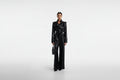 Sienna Noir women's jet black genuine Nappa lambskin leather jumpsuit featuring a trench coat style notch collar, chest storm flap, shoulder epaulettes, self-tie leather waist belt, wide-leg trousers, and custom made-to-measure fitting across the UK, USA, and Australia.